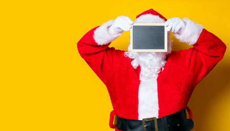Funny Santa Claus holding black board on yellow backgroundの写真素材
