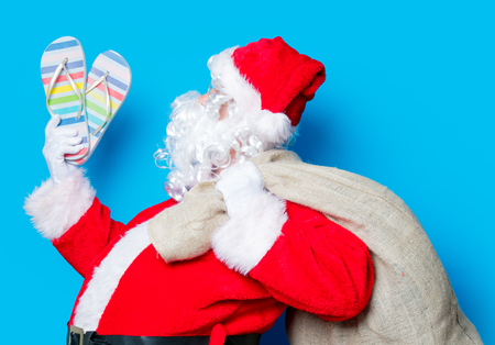 Funny Santa Claus have a fun with flip flops on blue backgroundの写真素材