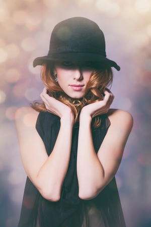Portrait of young redhead woman in black dress on background with bokeh