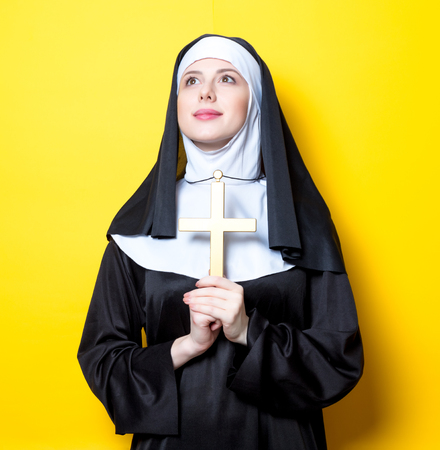 Young serious nun with cross on yellow backgroundの写真素材