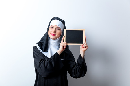 Young smiling nun with black board on white backgroundの写真素材