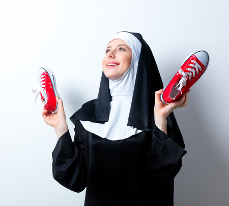 Young smiling nun with red gumshoes on white backgroundの写真素材