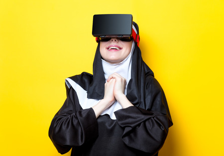 Young happy nun with Virtual Reality Glasses on yellow backgroundの写真素材