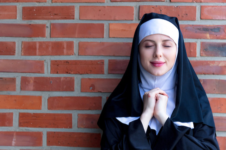 Young smiling nun on red brick wall backgroundの写真素材