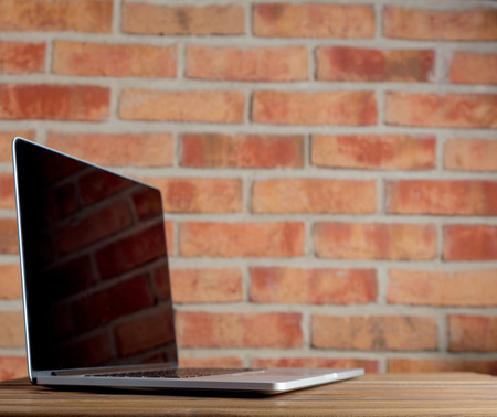 Modern laptop on wooden table and brick wall backgroundの写真素材
