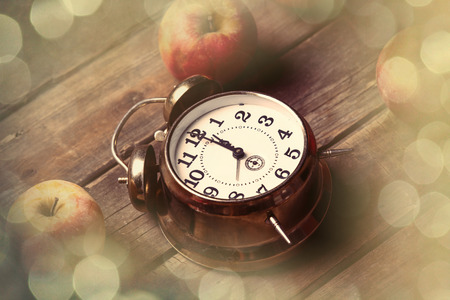 photo of the delicious apples and clock on the brown wooden background. Photo im old color image...