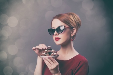 photo of beautiful young woman with plate full of chocolate candies on grey bokeh backgroundの写真素材