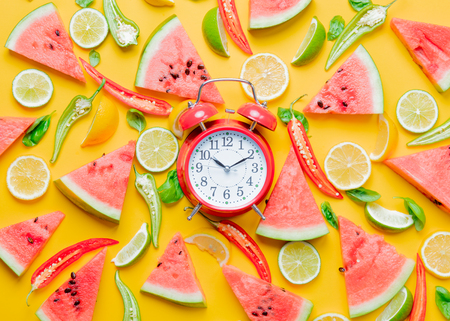 Above view at Watermelon and Chili pepper with lemons near alarm clock on yellow background