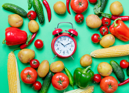 Above view at tomatoes and potatoes with alarm clock and vegetables on green backgroundの写真素材