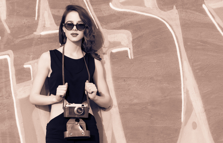 Beautiful redhead women with retro camera in black dress on graffiti background.の写真素材
