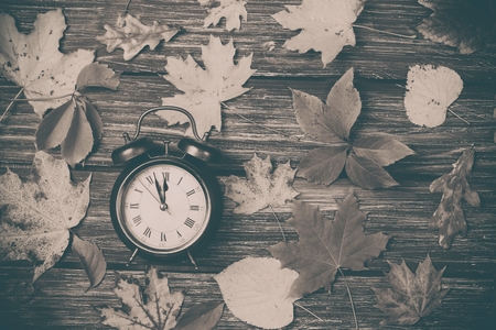 Autumn leaves and alarm clock on wooden table. Photo in old color image styleの写真素材