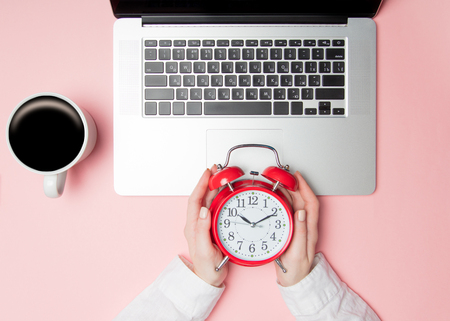Businesswoman holding alarm clock near laptop computer on pink backgroundの写真素材