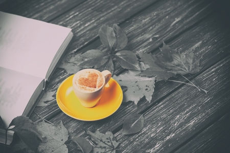 Autumn leaves, book and coffee cup on wooden table.の写真素材