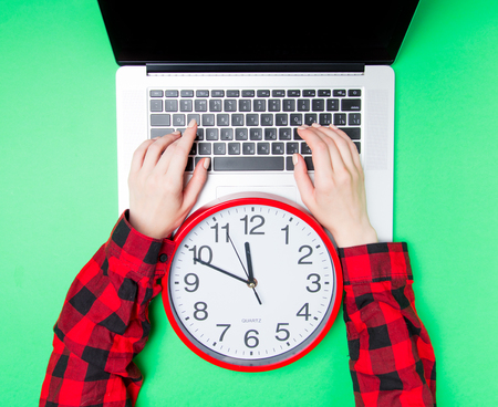 Female hands and big clock near laptop on green background