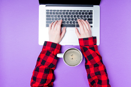Businesswoman hands with laptop and cup of coffee on purple background. Above viewの写真素材