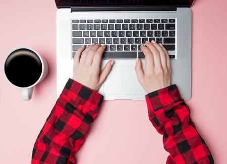 Freelancer woman typing on laptop near cup of coffee on pink backgroundの写真素材