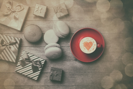 Cup of Cappuccino with heart shape symbol and gift boxes with macaron on wooden backgroundの写真素材