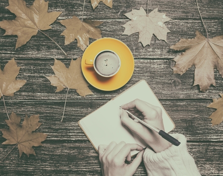 Female hand writing something in notebook near cup of coffee and autumn maple leavesの写真素材