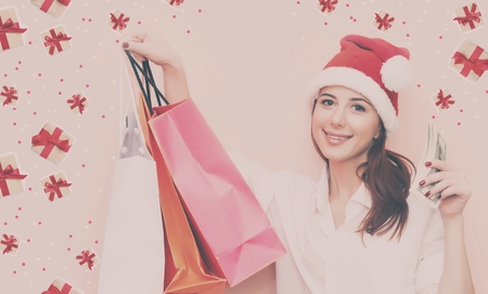 Portrait of a smiling redhead woman in Santa Claus hat with shopping bags on yellow backgroundの写真素材