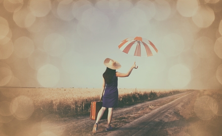 girl with suitcase and umbrella at countryside roadの写真素材