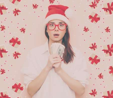 Portrait of surprised redhead woman in Santa Claus hat with money on pink backgroundの写真素材