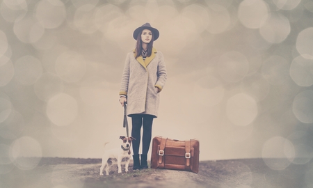 portrait of a young beautiful woman with suitcase and dog standing in the fieldの写真素材