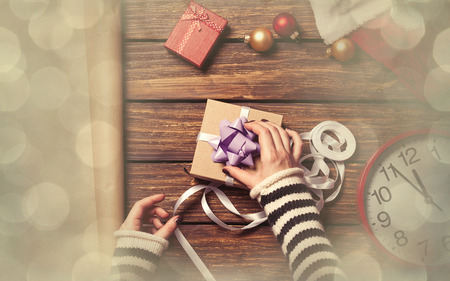 Female hands are wrapping a christmas gift on wooden backgroundの写真素材