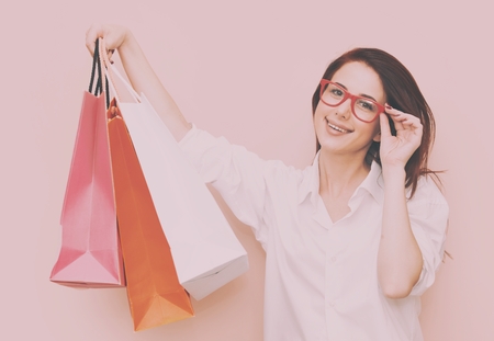 Portrait of smiling redhead woman with shopping bags on pink backgroundの写真素材