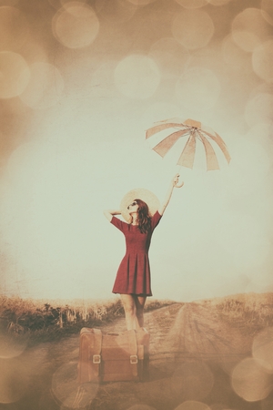 Redhead girl with suitcase and umbrella at countryside roadの写真素材