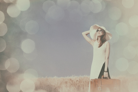 Redhead girl with suitcase at countryside road near wheat field.