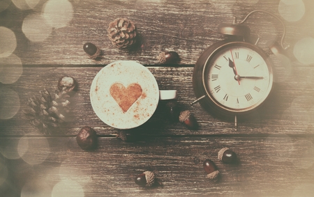 Cup of coffee with heart shape and pine cone with acorn and clock on wooden backgroundの写真素材