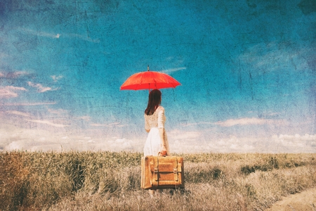 photo of young beautiful woman with suitcase and red umbrella in the fieldの写真素材