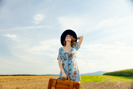 Portrait of young woman in dress at autumn countryside with suitcase.の写真素材