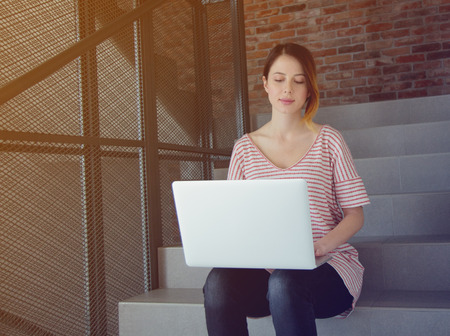 Beautiful young freelancer woman using laptop computer sitting at stairs inside the building.の写真素材