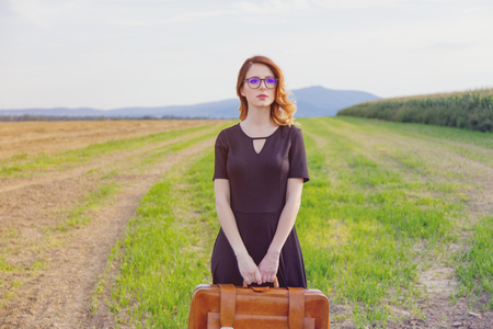 Portrait of young woman in black dress at autumn countryside with suitcase.の写真素材