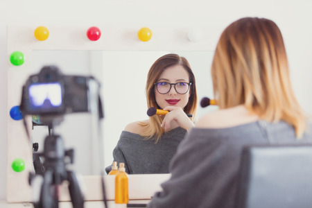 Young caucasian blogger woman applying cosmetics at camera for Video-sharing website. Home location near a mirrorの写真素材