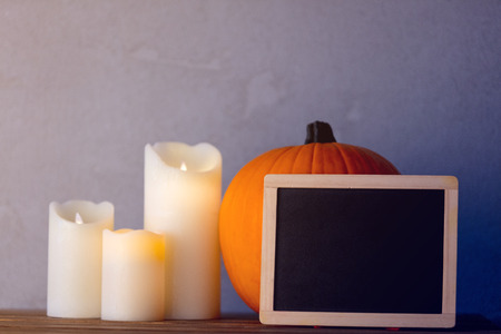 Orange Autumn pumpkin and candles with blackboard menu on wooden table near grey wall at backgroundの写真素材