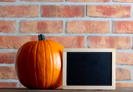 Autumn pumpkin and blackboard menu on wooden table with brick wall at backgroundの写真素材
