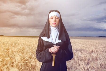 Young serious nun with cross on wheat field backgroundの写真素材