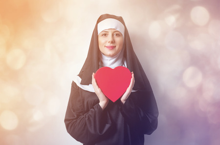 Young smiling nun with heart shape box on white backgroundの写真素材