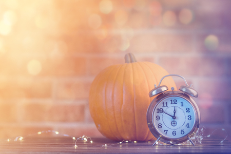 Autumn pumpkin with Fairy Lights and alarm clock at Halloween holiday on brick backgroundの写真素材