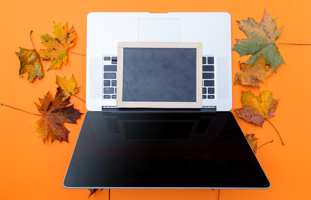 laptop computer and blackboard with autumn maple leaves aroung at orange backgroundの写真素材