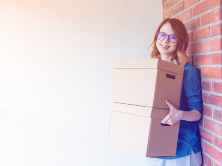 young redhead woman in jeans shirt standing on brick wall with moving boxes. European ethnicity