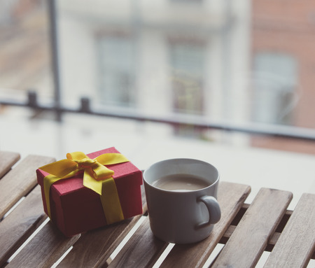 White cup of coffee or tea near a present gift on a wooden table near a window in rainy dayの写真素材