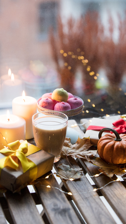 cup of coffee or tea near a pumpkin, gifts and candles with maple leaves and Fairy Lights  around on a wooden table near a window in rainy day. Autumn season imageの写真素材