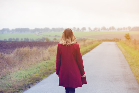 Back side view at redhead woman in red coat at countryside in autumn seasonの写真素材