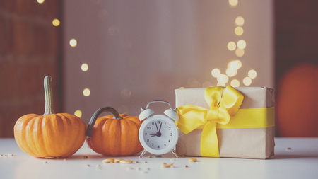 Retro alarm clock with pumpkins and gift box near Fairy Lights on backgroundの写真素材