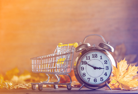 Vintage alarm clock and maple tree leaves with cart on yellow wooden background with bokeh.の写真素材