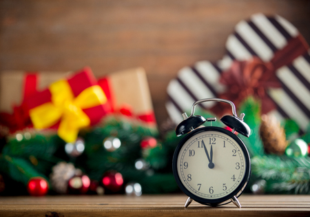 Alarm clock on wooden table with Christmas gifts and pine on backgroundの写真素材