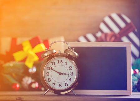 Alarm clock and blackboard on wooden table with Christmas gifts and pine on backgroundの写真素材